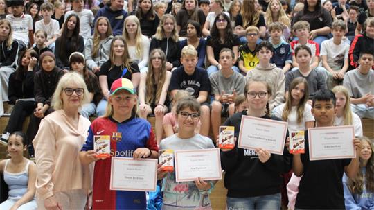 Gruppe von Jugendlichen in einer Turnhalle, vier von ihnen halten Urkunden und Bücher, eine Frau steht links neben ihnen