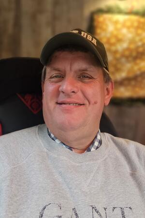 Glühwein & Co. auf dem Weihnachtsmarkt: Was kostet was? Konrad Ahrendt sitzt mit einer schwarzen Capi und einen grauen Pullover auf einem Stuhl.