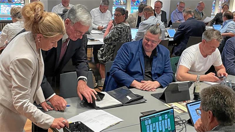 Mehrere Personen sitzen an einem Tisch und arbeiten mit Tablets und Papierunterlagen in einem hellen Raum