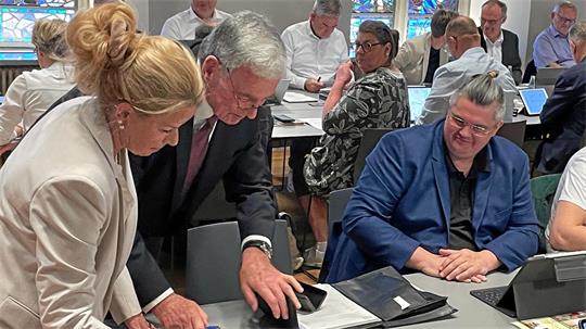 Mehrere Personen sitzen an einem Tisch und arbeiten mit Tablets und Papierunterlagen in einem hellen Raum