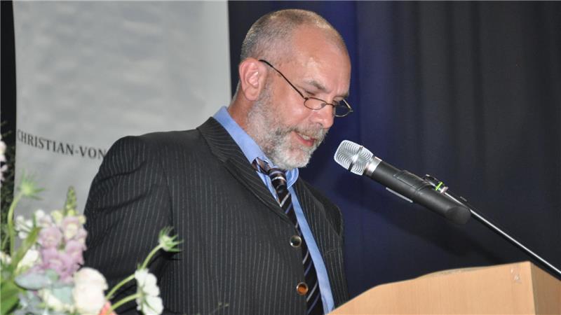 Ein Mann im dunklen Anzug mit Krawatte steht an einem Rednerpult vor einem Mikrofon.