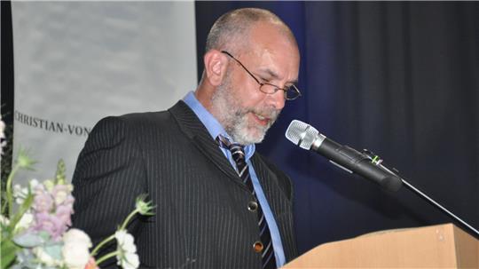 Ein Mann im dunklen Anzug mit Krawatte steht an einem Rednerpult vor einem Mikrofon.