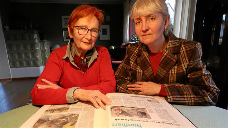 Zwei Frauen blättern in einem Album mit Zeitungsausschnitten.