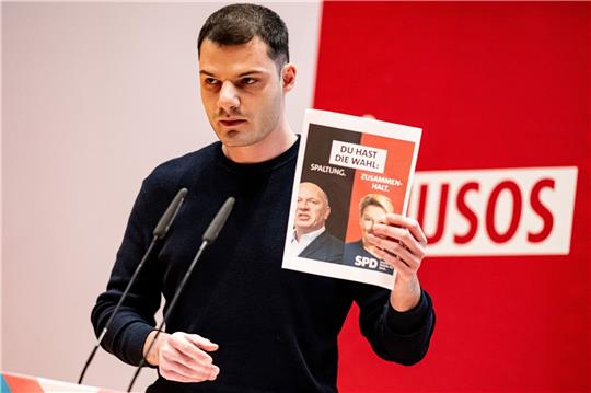 Kubilay Yalcin, Delegierter, hält auf der Landesdelegiertenkonferenz der Jusos Berlin ein Wahlplakat mit Giffey und Wegner in die Höhe.