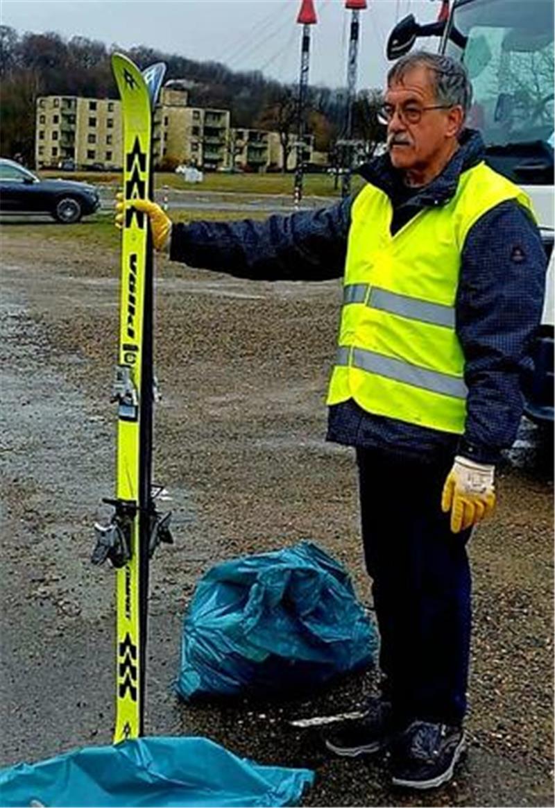„Müllboss“ in Goslar: Skier, Auspuff und „Drogen“ im Müll entdeckt Person mit gelber Warnweste und Handschuhen hält einen gelben Ski auf einem Parkplatz neben blauen Säcken.