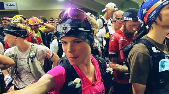 Gruppe von Sportlern mit Stirnlampen und Sportbekleidung in einem Innenraum, eine Frau im Vordergrund macht ein Selfie