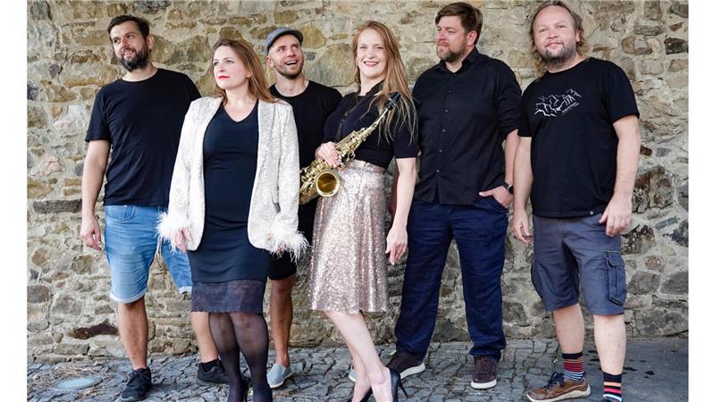 Sechs Menschen, eine Frau hat ein Saxophon umgehängt. 