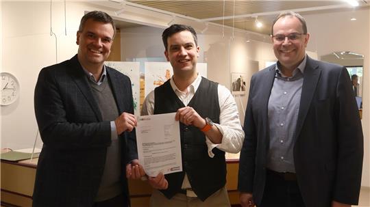Deutsch: 
kopieren
Drei Männer in Geschäftskleidung stehen in einem Büro, der mittlere hält ein Blatt Papier.