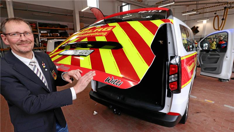 Ein Mann hält die Heckklappe eines Transporters, die in den reflektierenden Farben gelb und rot foliert ist.