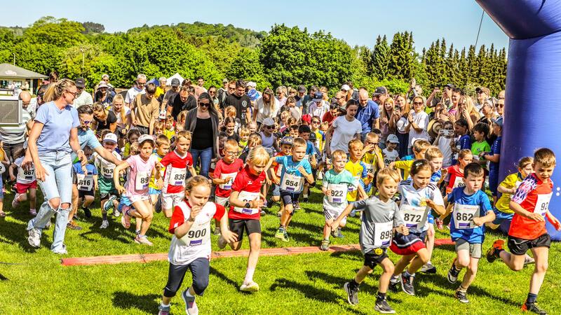 Kinder in Sportkleidung starten ein Rennen auf einer Wiese vor einer großen Menschenmenge.
