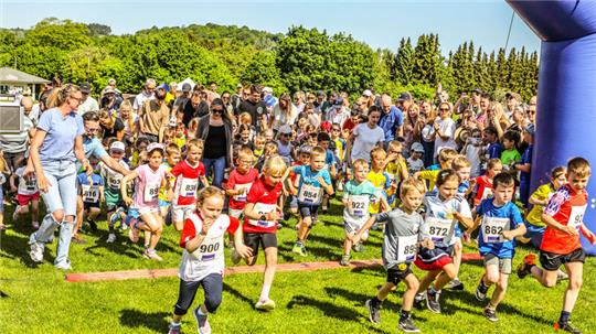 Kinder in Sportkleidung starten ein Rennen auf einer Wiese vor einer großen Menschenmenge.