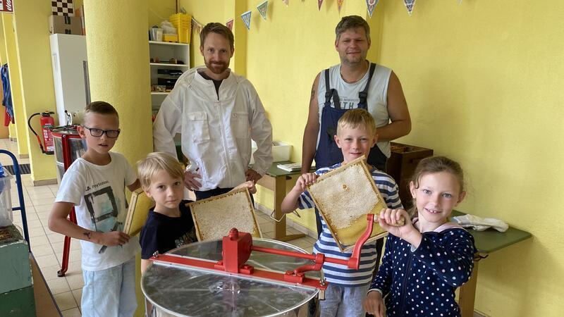Drittklässler ernten Honig und Viertklässler hören Klassik Lehrer und Imker Heiko Gerlach (li.) und Imker Thorben Falkenberg lösen mit Laura, Jonathan, Joschi und Lukas (v.r.) den frischen Honig aus den Wabenrahmen und bereiten die erste Schleuderrunde vor.