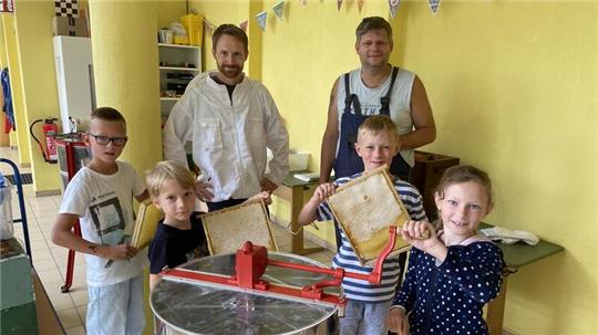Lehrer und Imker Heiko Gerlach (li.) und Imker Thorben Falkenberg lösen mit Laura, Jonathan, Joschi und Lukas (v.r.) den frischen Honig aus den Wabenrahmen und bereiten die erste Schleuderrunde vor.