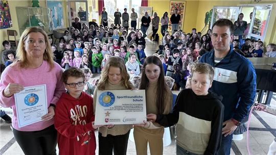 Lehrerin Kirsten Kretschmer (l.) und die Kinder der Grundschule Harlingerode sind stolz auf das Zertifikat, das ihnen Florian Schütte vom „Regionalen Landesamtes für Bildung und Schule“ überreicht.