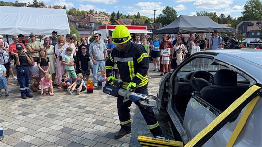 Das Foto zeigt einen Mann, der vor vielen Zuschauern mit einem schweren Gerät ein Auto zerstört. 