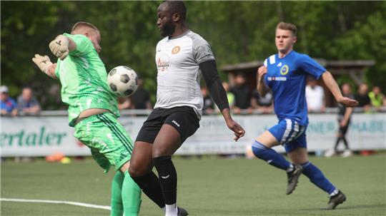 Drei Fußballspieler auf dem Spielfeld, einer in grün springt zum Ball, ein weiterer in weiß steht davor, ein dritter in blau läuft im Hintergrund
