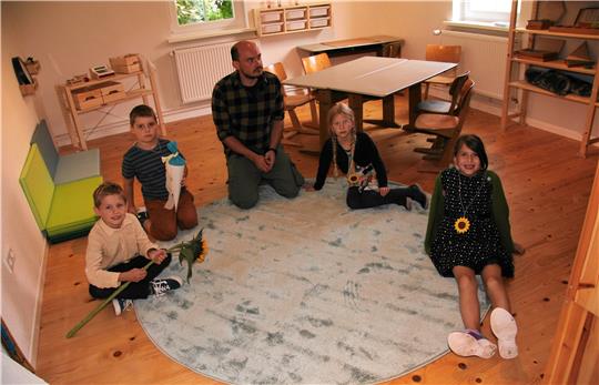 Lernbegleiter Adrian Bothe sitzt mit Kindern in einem Schulraum.  Foto: Hohaus