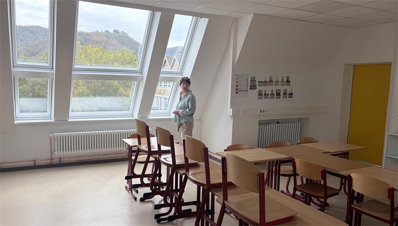 Das Foto zeigt eine Frau, die in einem Klassenzimmer am Fenster steht.
