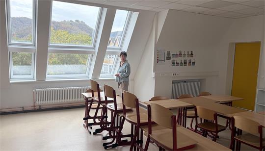 Das Foto zeigt eine Frau, die in einem Klassenzimmer am Fenster steht.