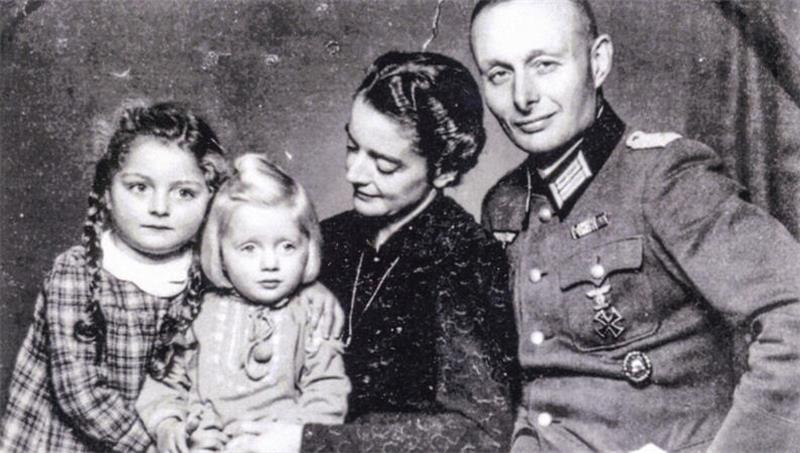 Schwarz-weiß-Familienporträt mit zwei Kindern, einer Frau und einem Mann in Uniform, die nebeneinandersitzen.