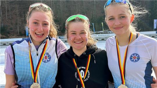 Drei junge Frauen mit Medaillen um den Hals stehen nebeneinander vor einem Wald im Hintergrund.