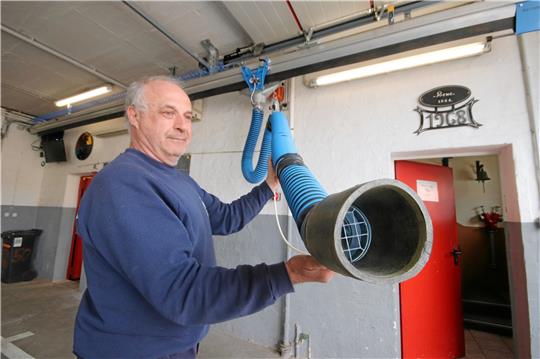 Löschmeister Frank Jannaschk präsentiert den Absaugrüssel. Die verbaute Führungsschiene unter der Decke ist länger als nötig, um sie wiederverwenden zu können.