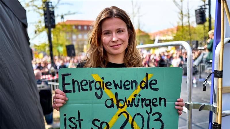 Luisa Neubauer hält ein Schild mit der Aufschrift „Energiewende abwürgen ist so 2013“ in der Hand. 
