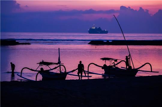 Männer befestigen vor Sonnenaufgang am Tag vor Beginn des G20-Gipfels am Strand von Nusa Dua Boote, wobei im Hintergrund ein Schiff der indonesischen Marine zu sehen ist.