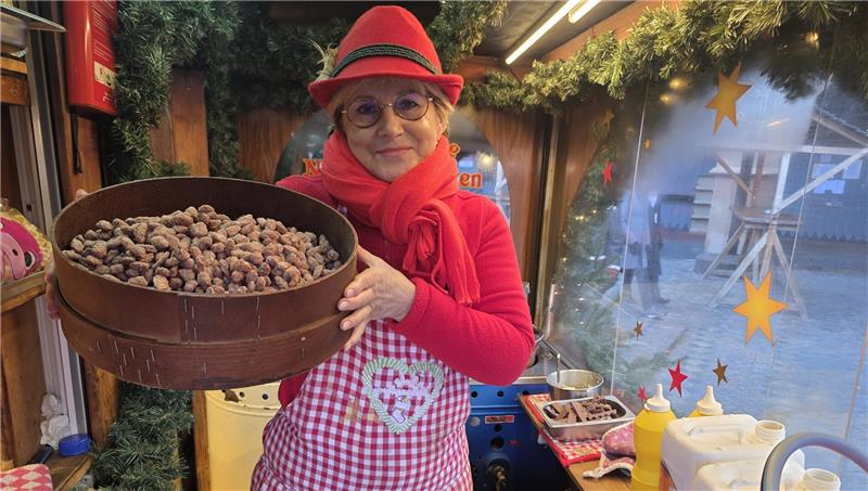 Das sagen die Schausteller zum Goslarer Weihnachtsmarkt Person in rotem Pullover, rotem Hut und rot-weiß kariertem Latzkleid hält ein rundes Holzgefäß mit gebrannten Mandeln in einer Weihnachtsmarkt-Hütte.