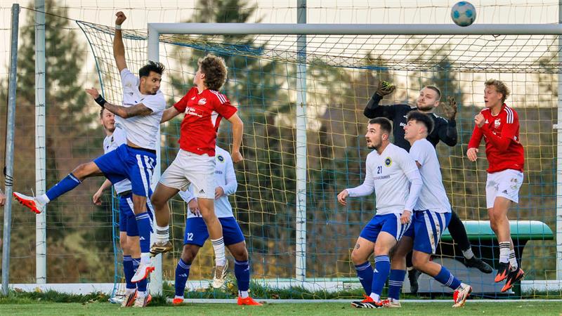 Fußballspieler springen im Strafraum vor dem Tor, um den Ball zu erreichen, während der Torwart bereitsteht