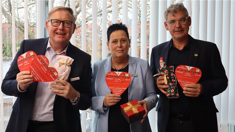 Drei Menschen halten rote Herzen und Weihnachtstüten in die Kamera. 