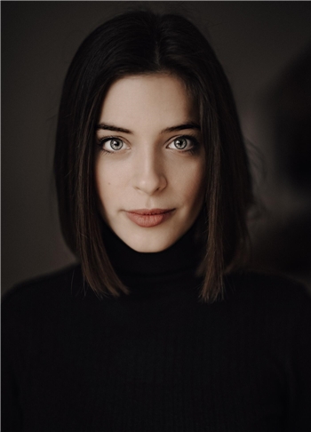 Weibliche Person mit schulterlangem, glattem Haar trägt schwarzen Rollkragenpullover vor dunklem Hintergrund.