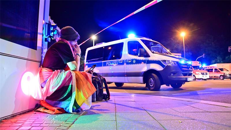 Marlon ist in eine Pride-Fahne gehüllt und hockt neben einem Polizeifahrzeug nach dem Abbruch des Christopher Street Day in Berlin. 