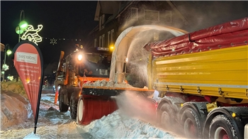 Das Foto zeigt eine Schneefräse, die Schnee auf die Ladefläche eines Lastwagen fräst.