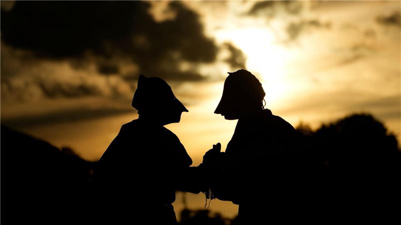 Maskierte Freischärler schauen sich bei Sonnenuntergang eine traditionelle Reitershow an.