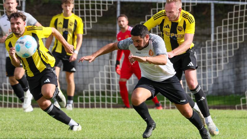 Fußballspieler in gelb-schwarzen Trikots und ein Spieler in weißem Trikot kämpfen um den Ball vor dem Tor