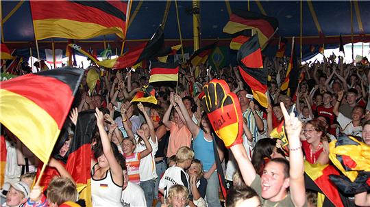 Menschenmenge in einem Zelt, die deutsche Fahnen schwenkt und jubelt