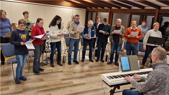 Mehr als Dutzend Hobby-Sängerinnen und Sänger machen in der Flambacher Mühle beim Workshop mit. Die Leitung übernimmt André Wenauer (am Piano). Foto: Knoke