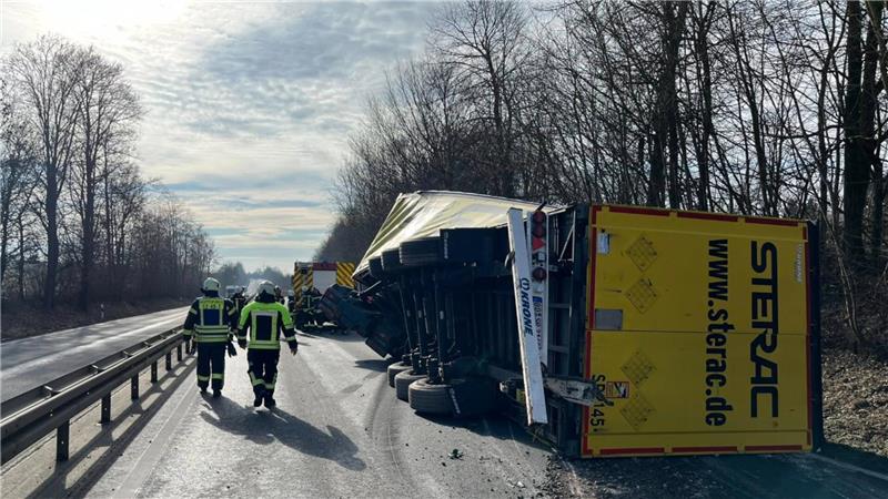 Feuerwehrmänner stehen an der Unfallstelle, ein Lkw ist auf die Seite gekippt