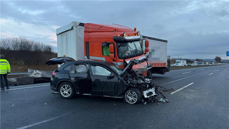 Ein Lkw steht schief hinter einem schwarzen, kaputten Auto auf einer Autobahn.