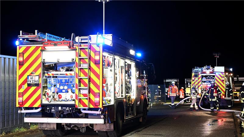 Zwei Feuerwehrfahrzeuge mit geöffneten Heckklappen und eingeschaltetem Blaulicht bei nächtlichem Einsatz, mehrere Feuerwehrleute in Einsatzkleidung stehen daneben