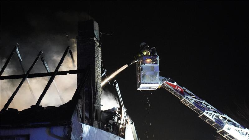 Ein Feuerwehrmann löscht von einer Drehleiter einen Dachstuhlbrand.