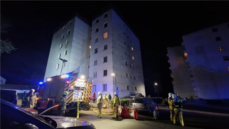 Mehrere Feuerwehrleute und ein Feuerwehrauto stehen vor dem betroffenen Haus. Dort kam es zu einem Brand im dritten Obergeschoss.