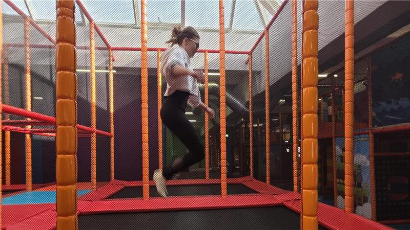 Person mit Brille springt in einem Trampolinpark zwischen orangefarbenen und roten Sicherheitsnetzen.