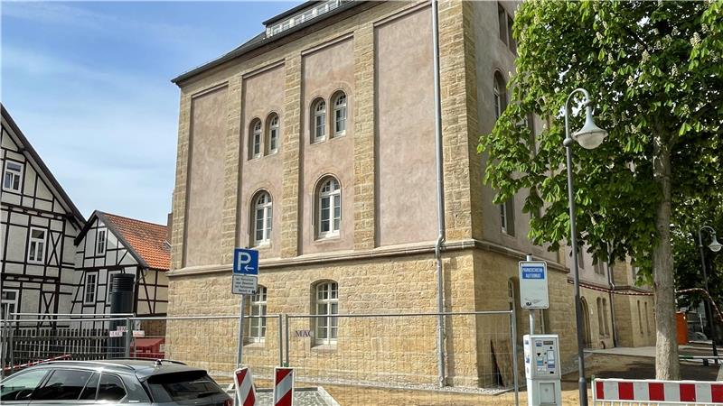 Straßenecke mit historischem Sandsteingebäude, parkenden Autos und Verkehrsschildern bei sonnigem Wetter
