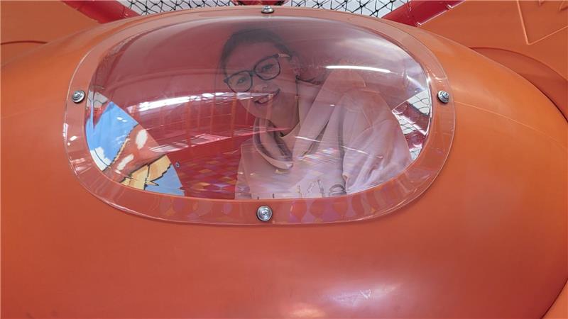 Person blickt durch die gewölbte Scheibe eines orangefarbenen Fahrzeugs oder Geräts.