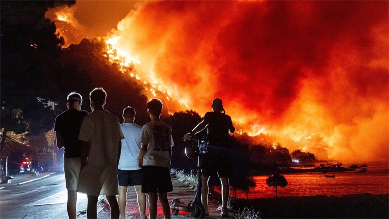 Menschen beobachten am frühen Freitag, dem 14. August 2026, einen Waldbrand an der Adriaküste in der Nähe von Omis im Süden Kroatiens.