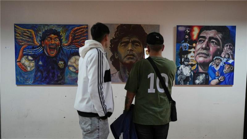 Menschen betrachten eine Kunstausstellung mit Bildern des verstorbenen Fußballstars Maradona.