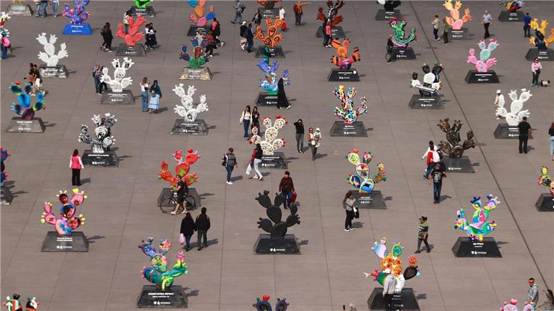 Menschen betrachten monumentalen Skulpturen in Form von Kakteen die von mexikanischen Künstlern gefertigt wurden.