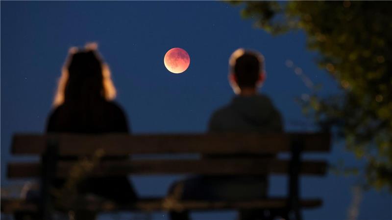 Bilder des Tages Menschen betrachten von einer Parkbank aus die auch als Blutmond bezeichnete totale Mondfinsternis in Leipzig.